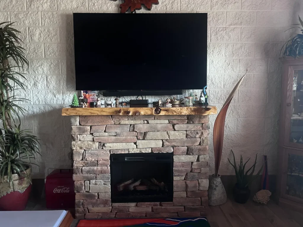 TV mounted above stone fireplace with rustic mantel in Shores Florida