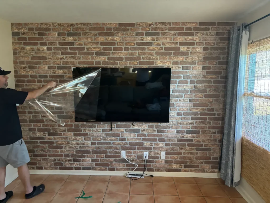 Removing protective film from TV mounted on brick accent wall in Shores Florida